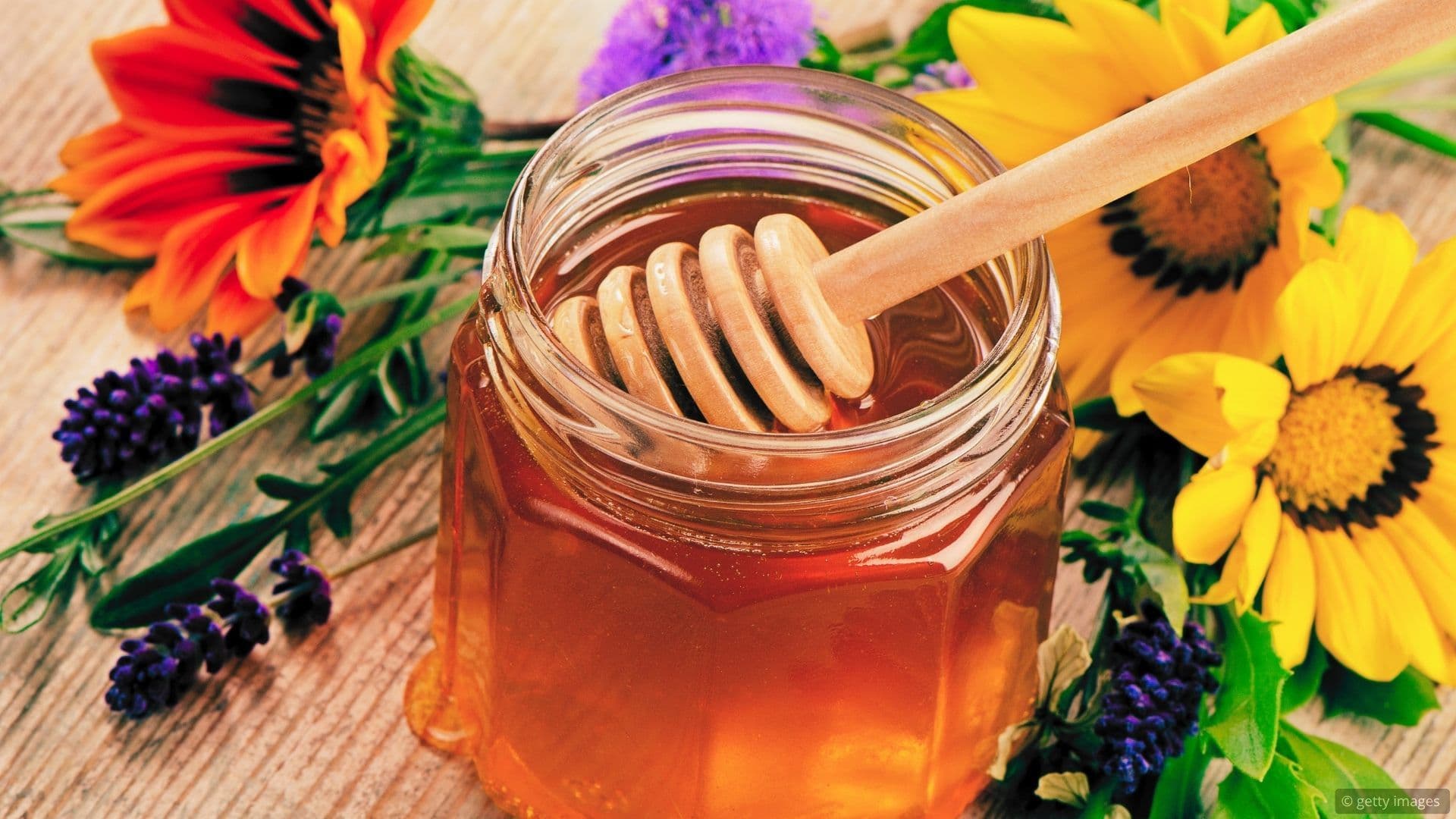 honey in a jar with flowers behind it